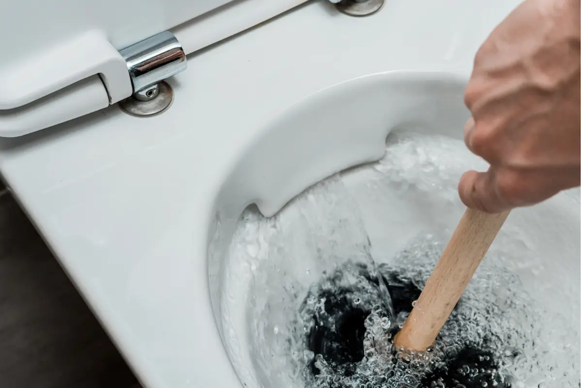 Imagem mostra uma pessoa usando um desentupidor improvisado dentro do vaso sanitário com água circulando enquanto tenta aprender como desentupir vaso de forma prática em casa.