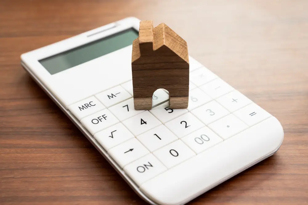 Miniatura de casa posicionada sobre uma calculadora simboliza o processo de calcular reajuste de aluguel, representando a atualização do valor do aluguel com base em índices econômicos.