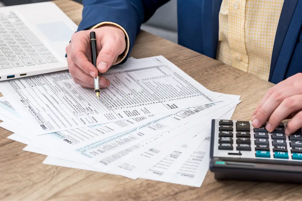 Pessoa analisa documentos financeiros e utiliza uma calculadora sobre a mesa para calcular reajuste de aluguel, verificando valores e índices enquanto revisa planilhas e contratos.
