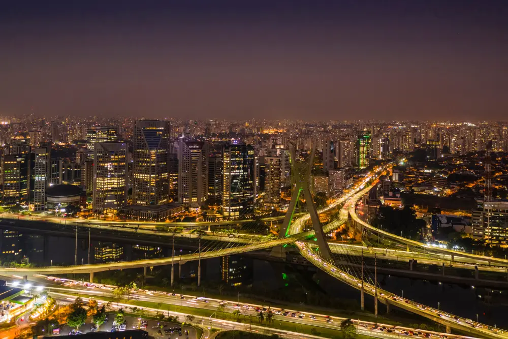 Vista aérea noturna de São Paulo com ponte estaiada iluminada, avenidas movimentadas e skyline urbano, representando o que fazer à noite em São Paulo com cenário vibrante urbano